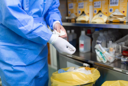 Healthcare workers handling biomedical waste with protective equipment and labeled disposal containers in a hospital setting.