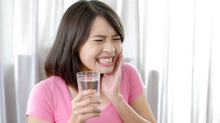 What Causes Sudden Tooth Sensitivity? Person experiencing sharp tooth sensitivity while drinking cold water.